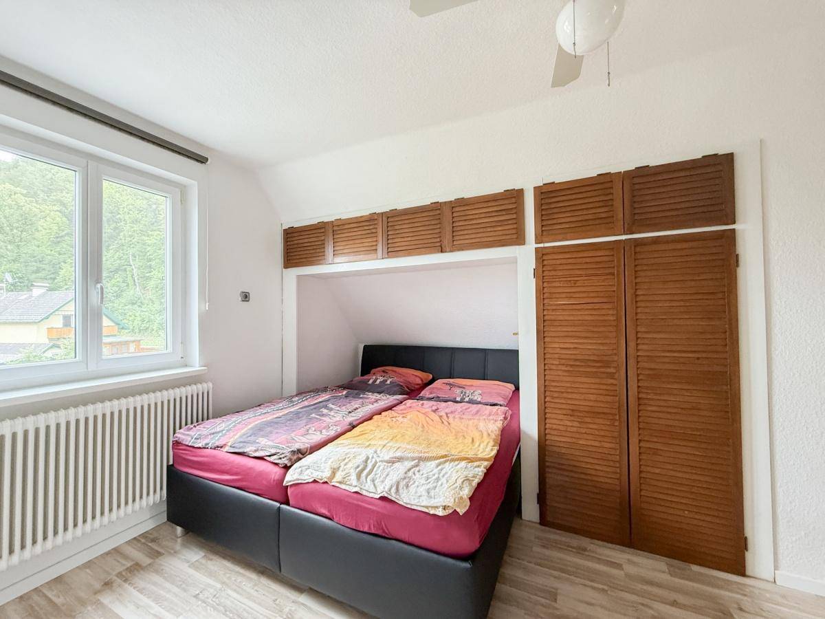 Schlafzimmer mit Doppelbett in einer Nische und integrierten Holzschränken sowie Laminatboden.