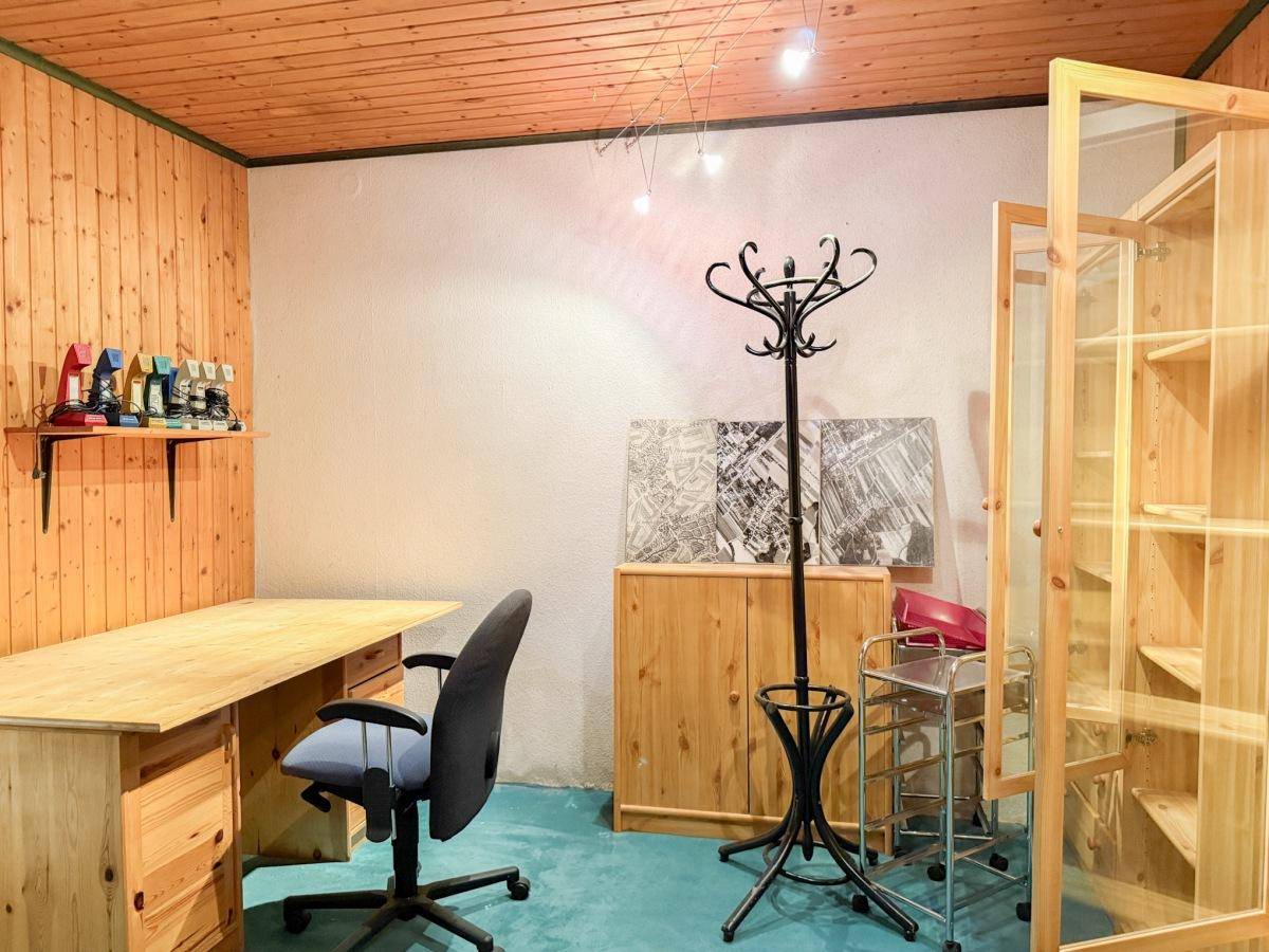Arbeitszimmer mit Holzschreibtisch, Bürostuhl, Garderobe und Holzvertäfelung an Wand und Decke.