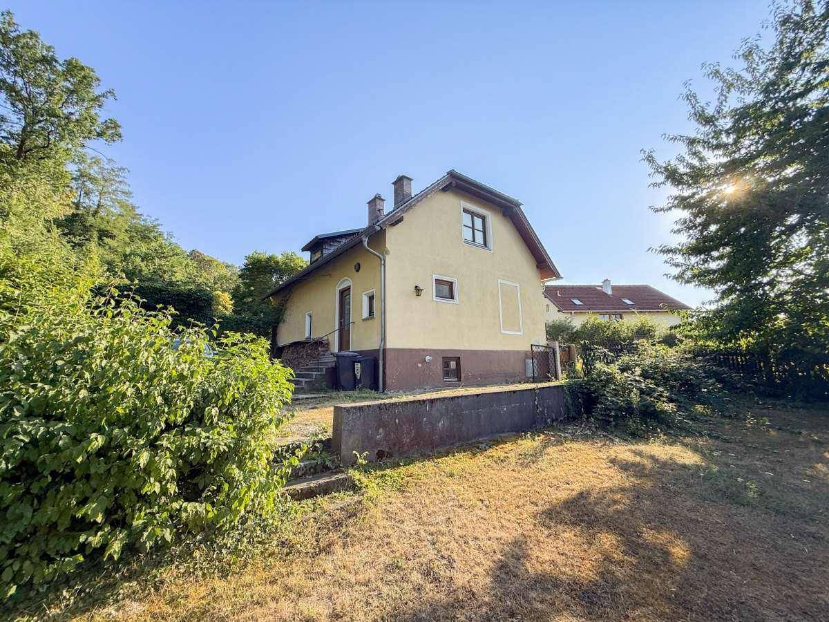 Seitenansicht des Hauses mit abfallendem Garten und viel Grün in der Umgebung.