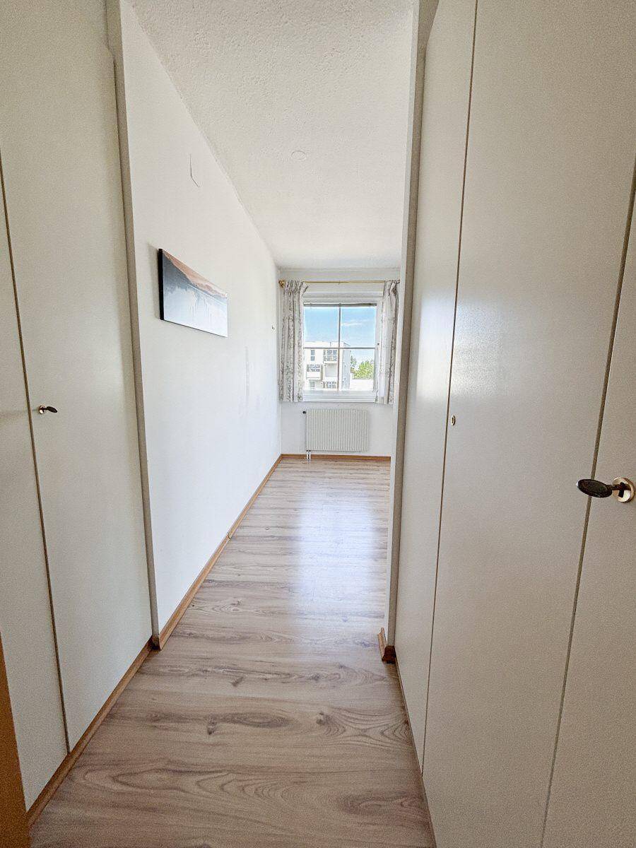 Schmaler Flur mit Laminatboden und Einbauschränken, der zu einem Fenster führt.