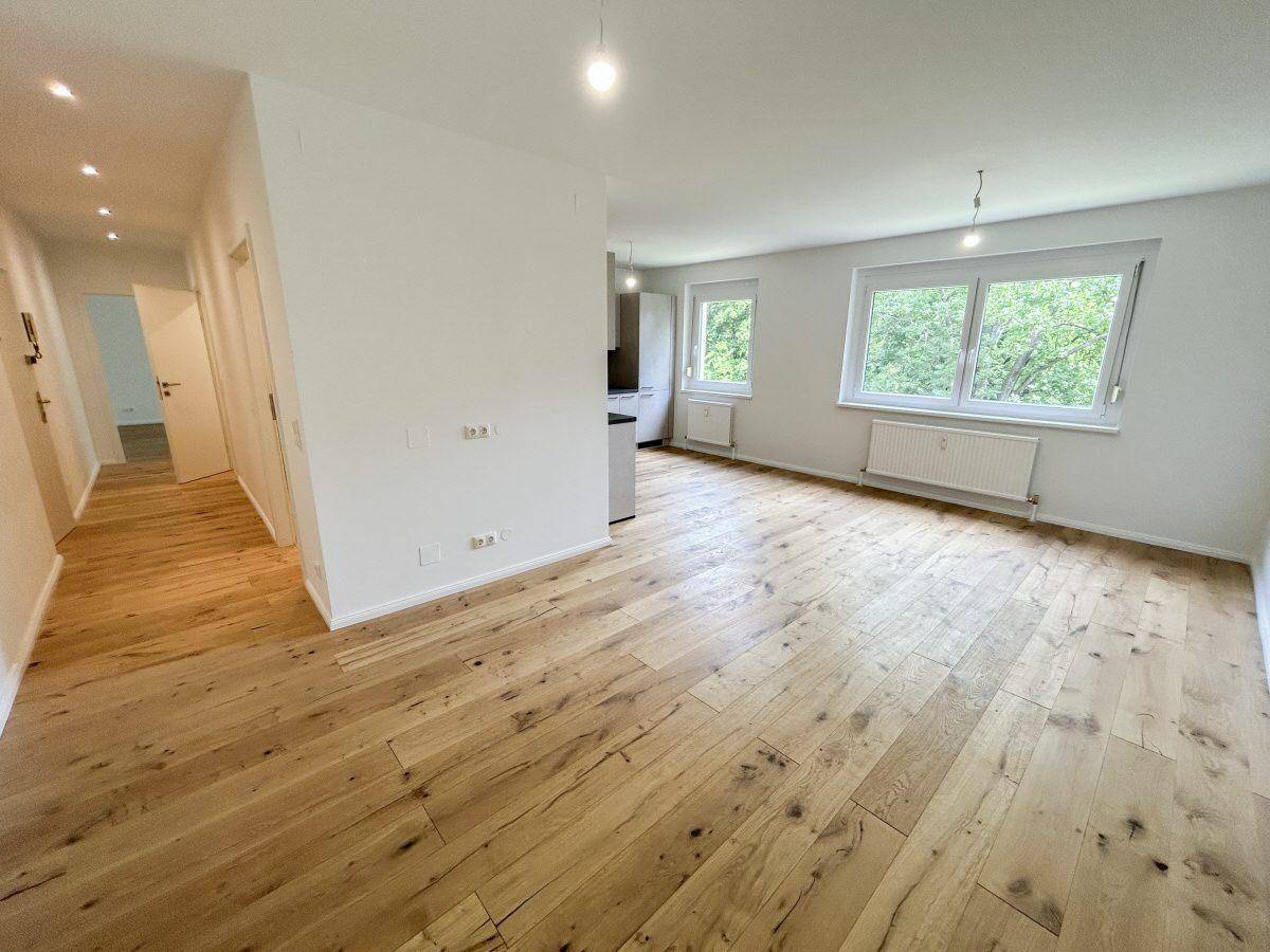 Helles Wohnzimmer mit neuem Holzboden und großen Fenstern mit Blick ins Grüne.