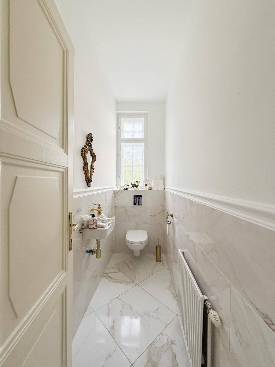 Schmale Gästetoilette mit Marmorfliesen, wandhängendem WC und kleinem Fenster.