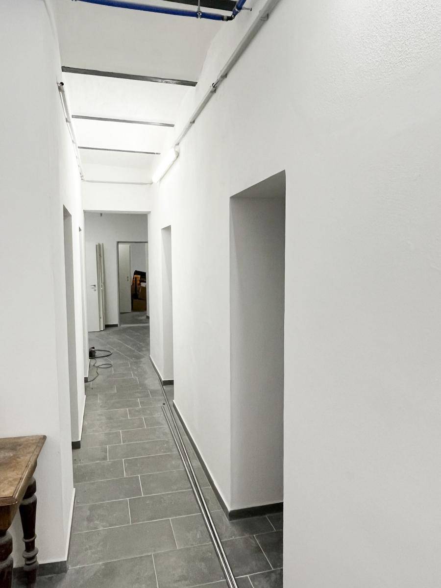 Heller Flur mit modernen grauen Fliesen und weißen Wänden, der zu verschiedenen Räumen führt.