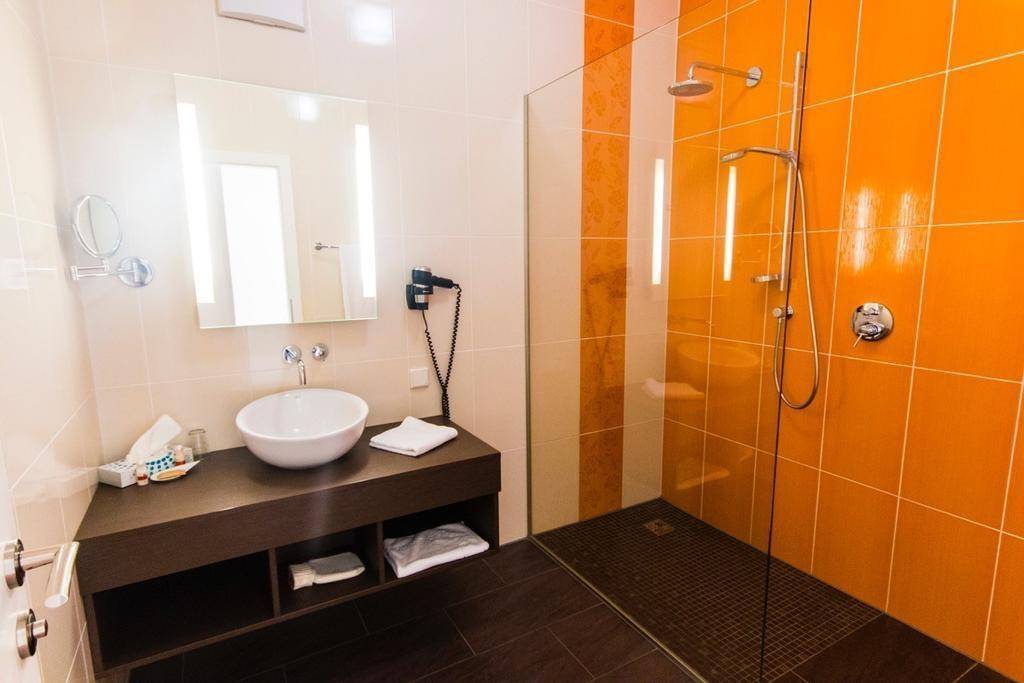 Modernes Badezimmer mit orangefarbenen Fliesen, ebenerdiger Dusche und Aufsatzwaschbecken.