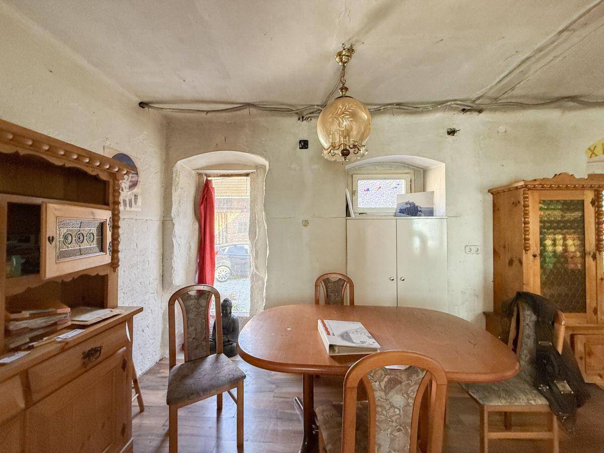 Esszimmer mit Holztisch, Stühlen und traditionellen Holzmöbeln, durch einen Bogen mit einem anderen Raum verbunden.