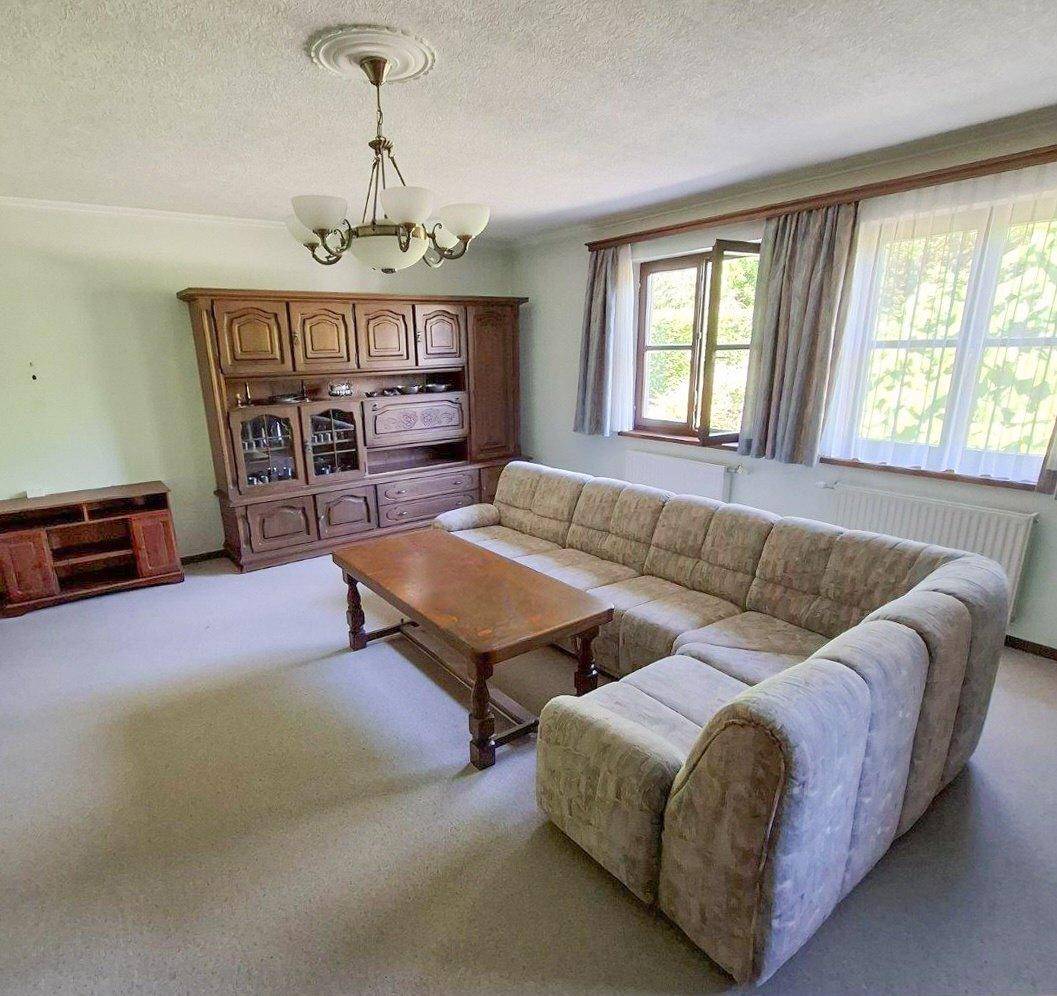 Geräumiges Wohnzimmer mit großem Ecksofa, traditionellem Holzschrank und Fenstern mit Tageslicht.