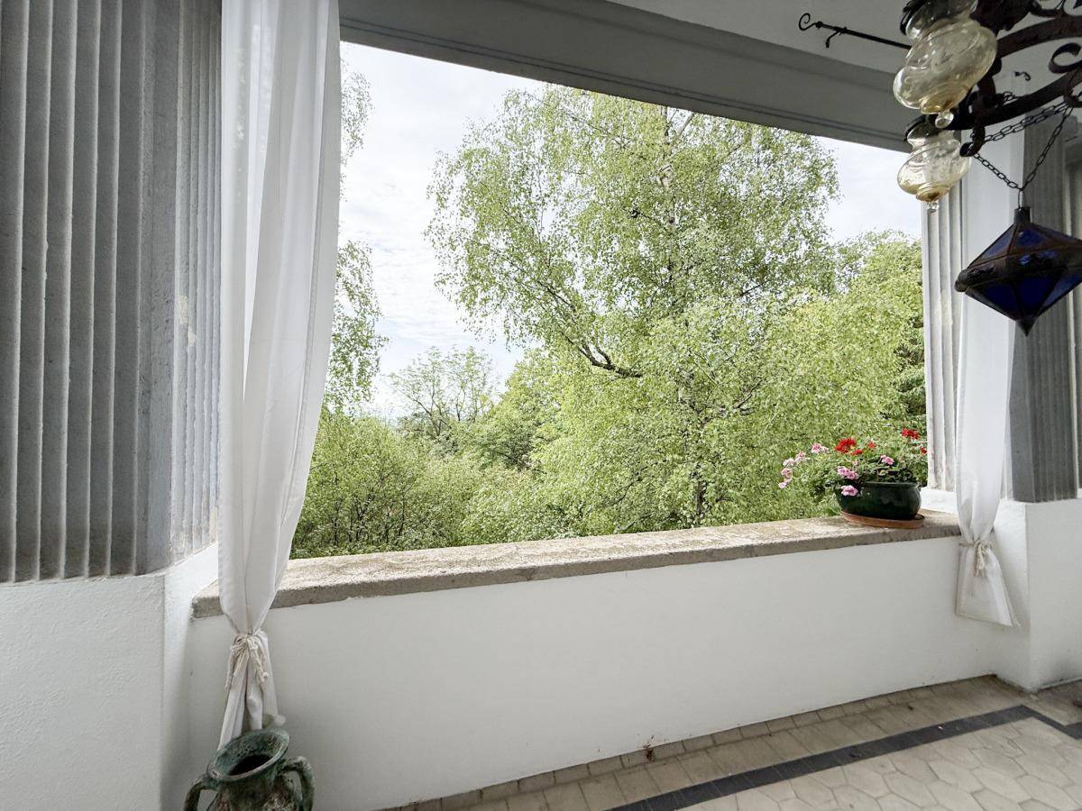 Blick von einem Balkon ins Grüne mit üppiger Vegetation und hellem Himmel.