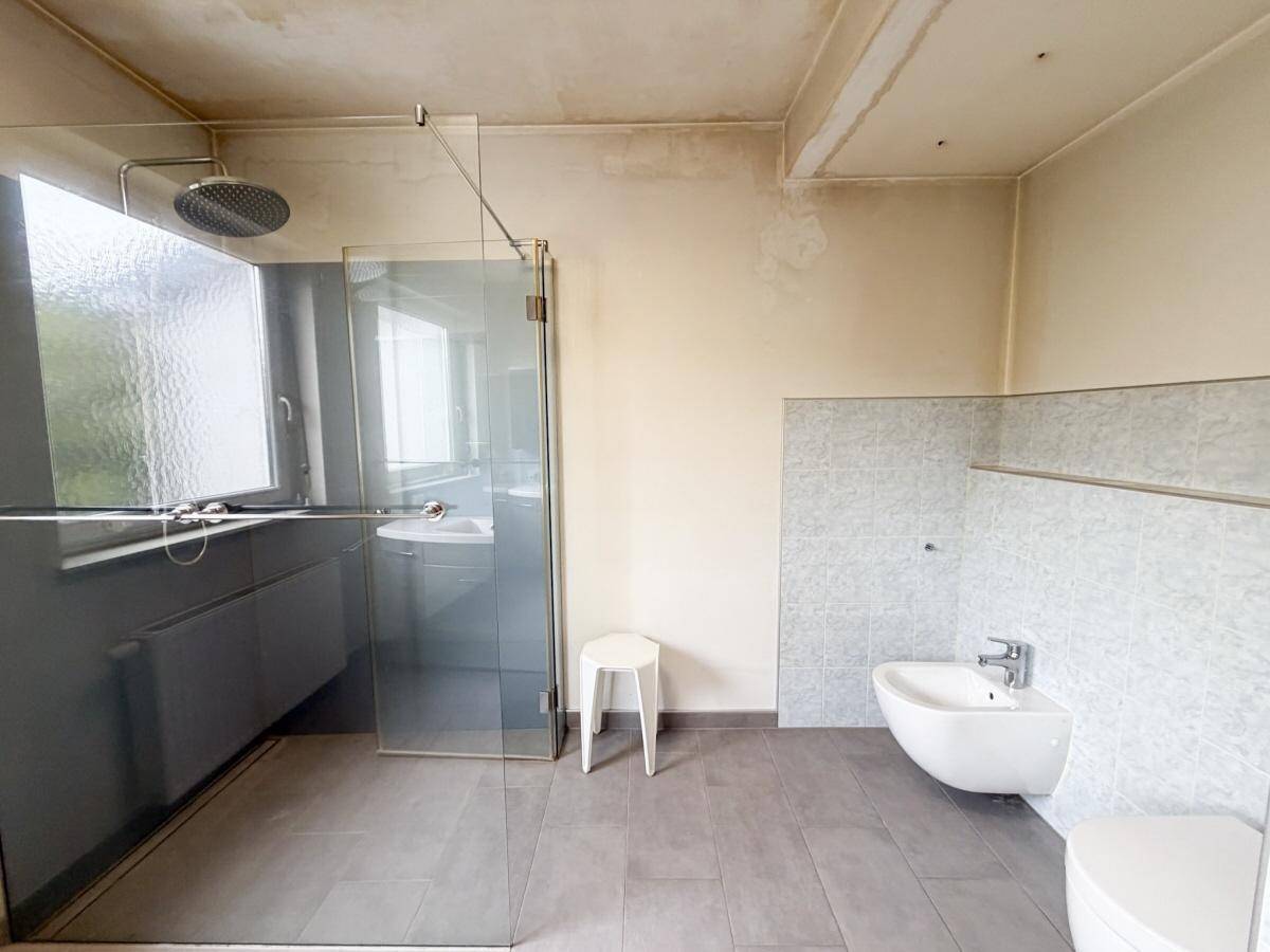 Modernes Badezimmer mit begehbarer Dusche, Bidet und großem Fenster.