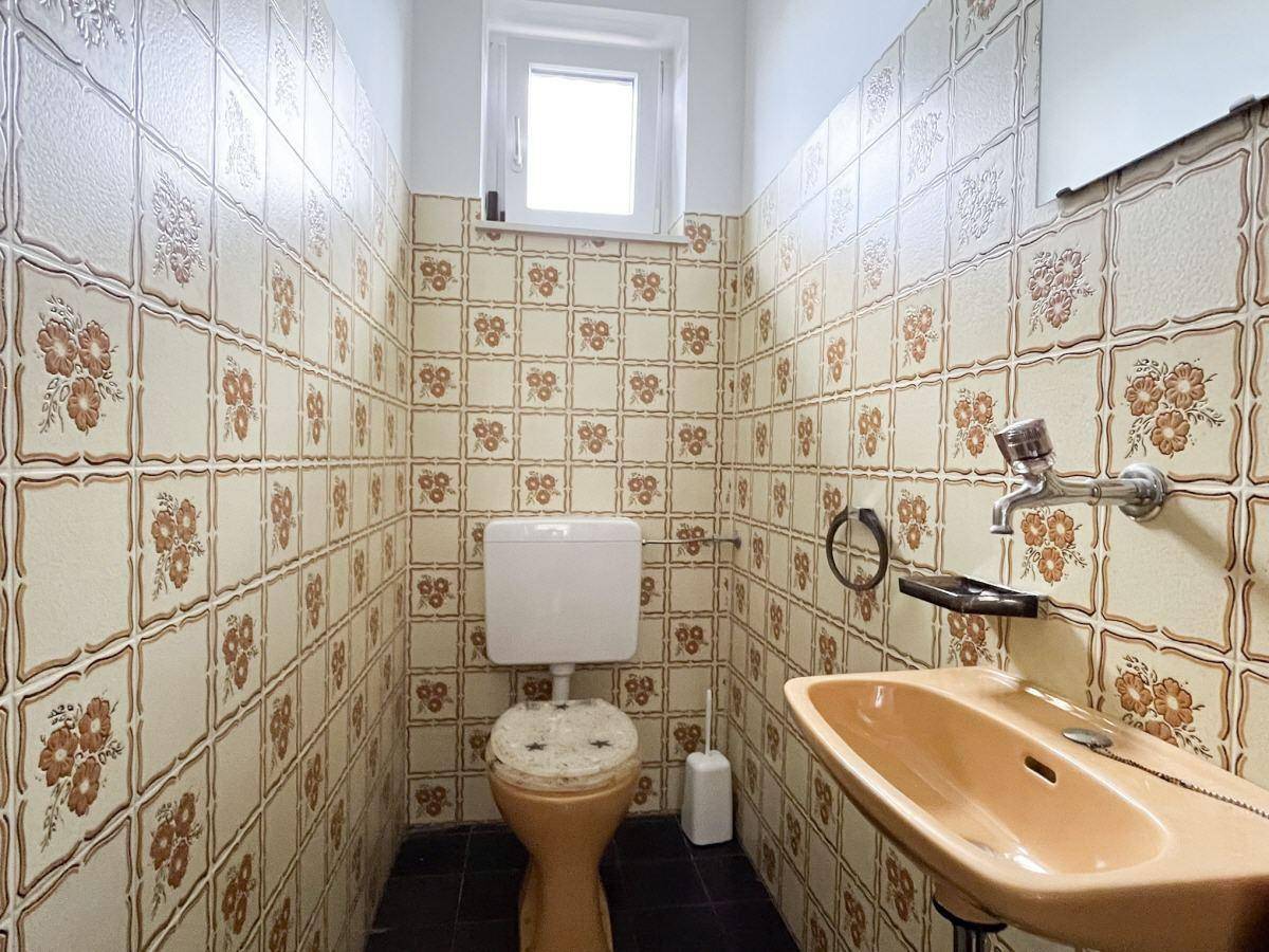Gäste-WC mit Fenster, farbigen Fliesen und einfacher Ausstattung.