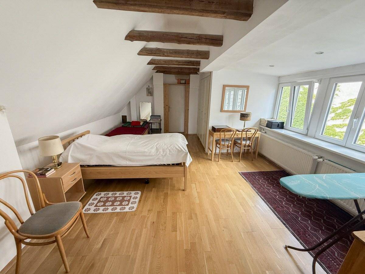 Geräumiges Schlafzimmer im Dachgeschoss mit Holzboden, sichtbaren Holzbalken und vielen Fenstern.