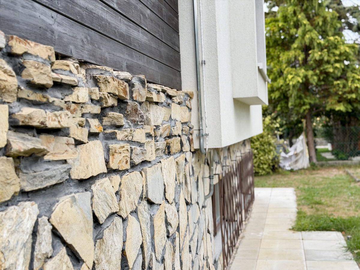 Detailansicht der Hausfassade mit Natursteinverkleidung und Holzpaneelen.