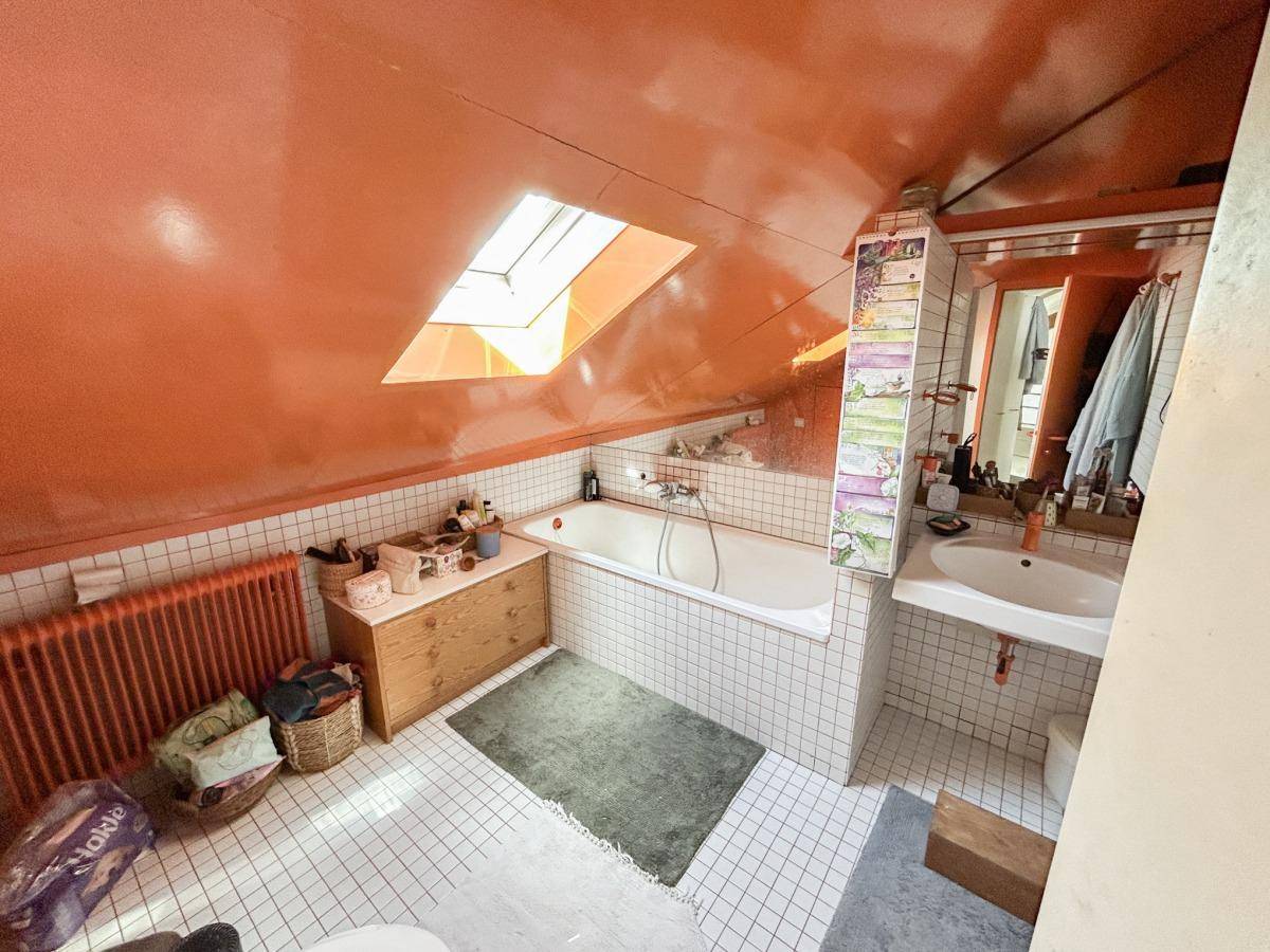 Badezimmer mit Badewanne, Dachfenster und auffälliger orangefarbener Decke.