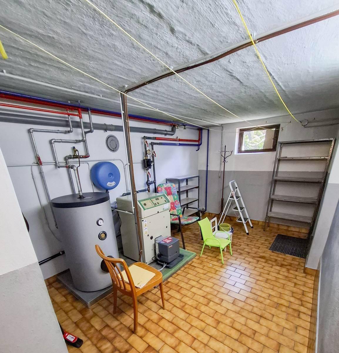Kellerraum mit Heizungsanlage, Warmwasserspeicher und Regalen für Lagerzwecke, funktional eingerichtet.