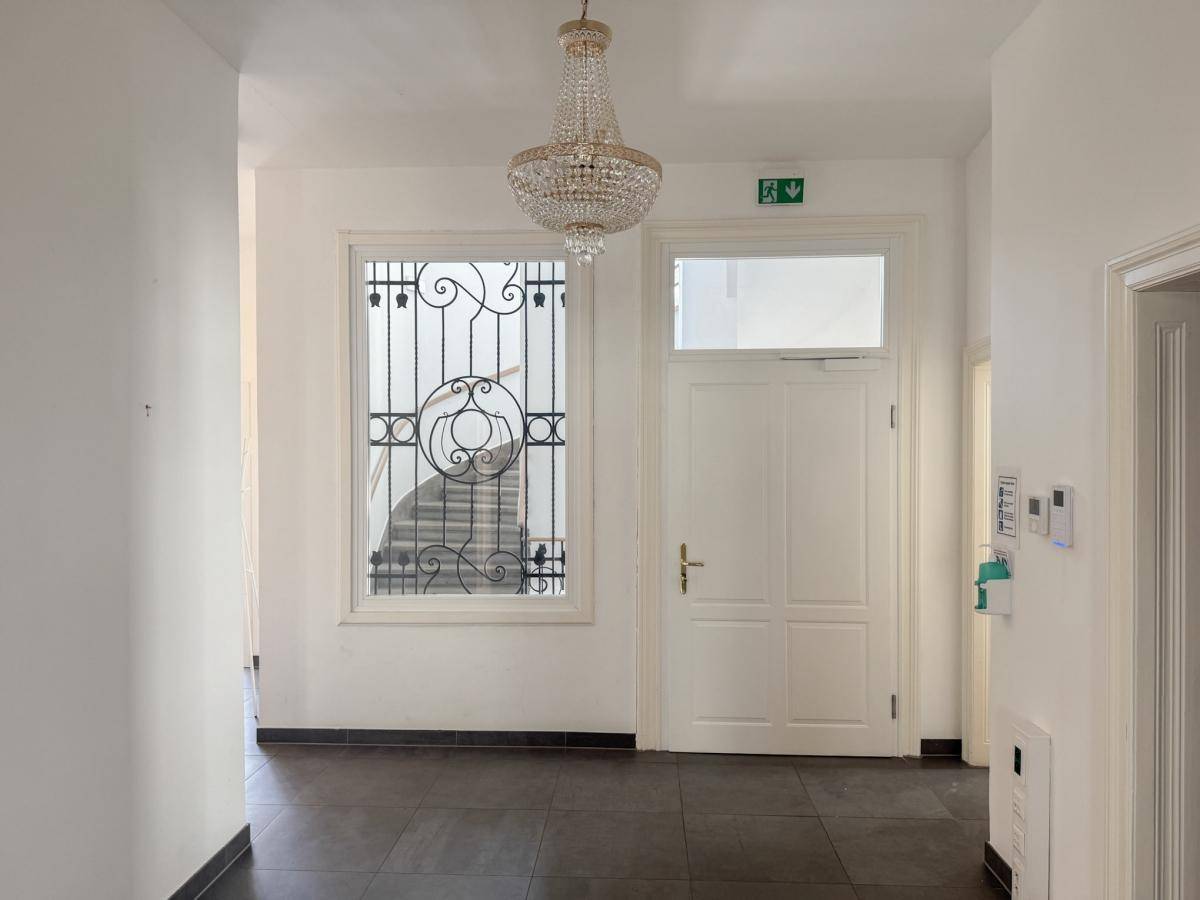 Eingangsbereich mit dunklem Fliesenboden, weißer Tür und einem dekorativen Fenster zum Treppenhaus.