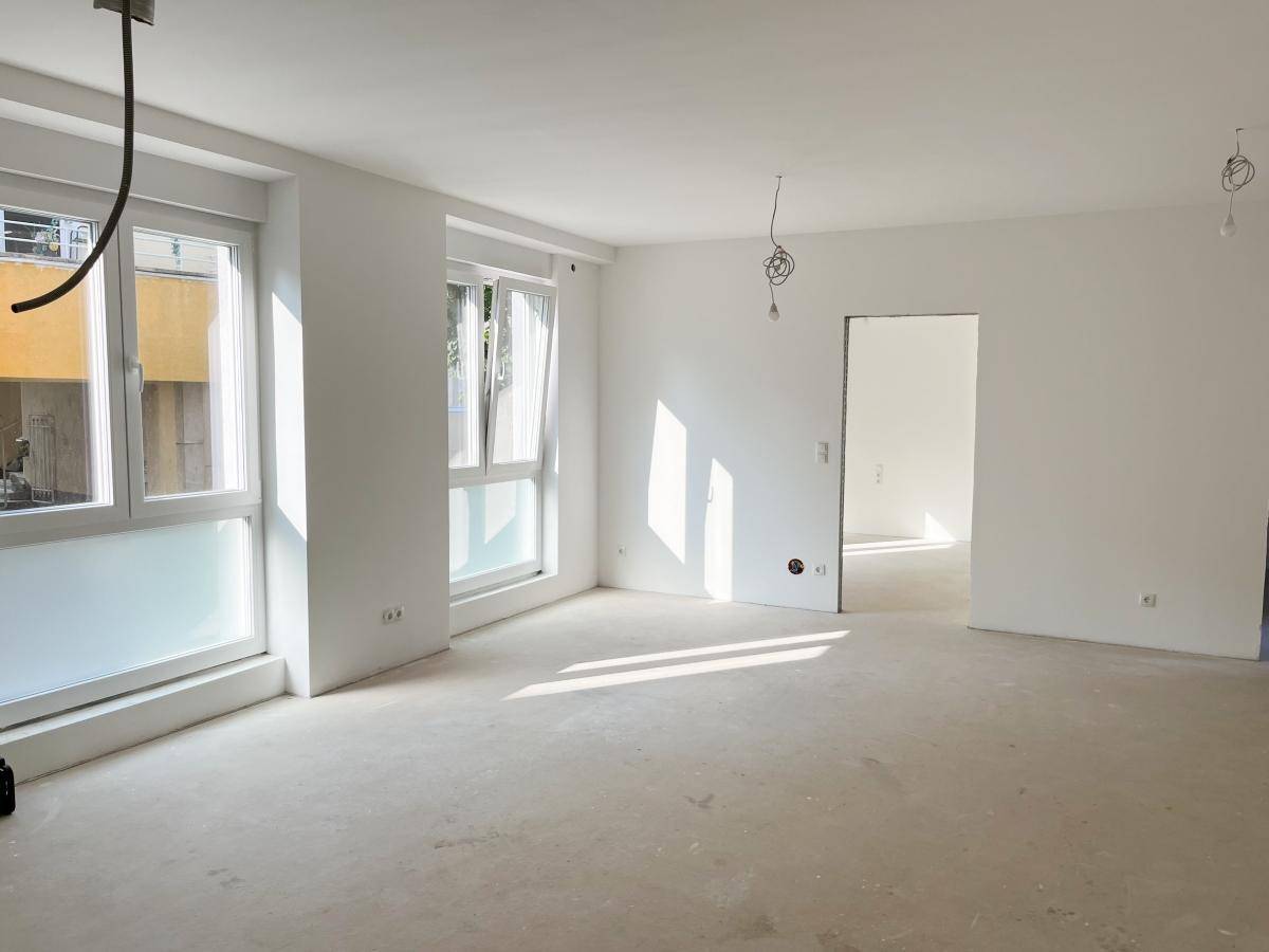 Geräumiger, heller Raum mit großen Fenstern und viel Sonnenlicht, ideal für Wohnzwecke.