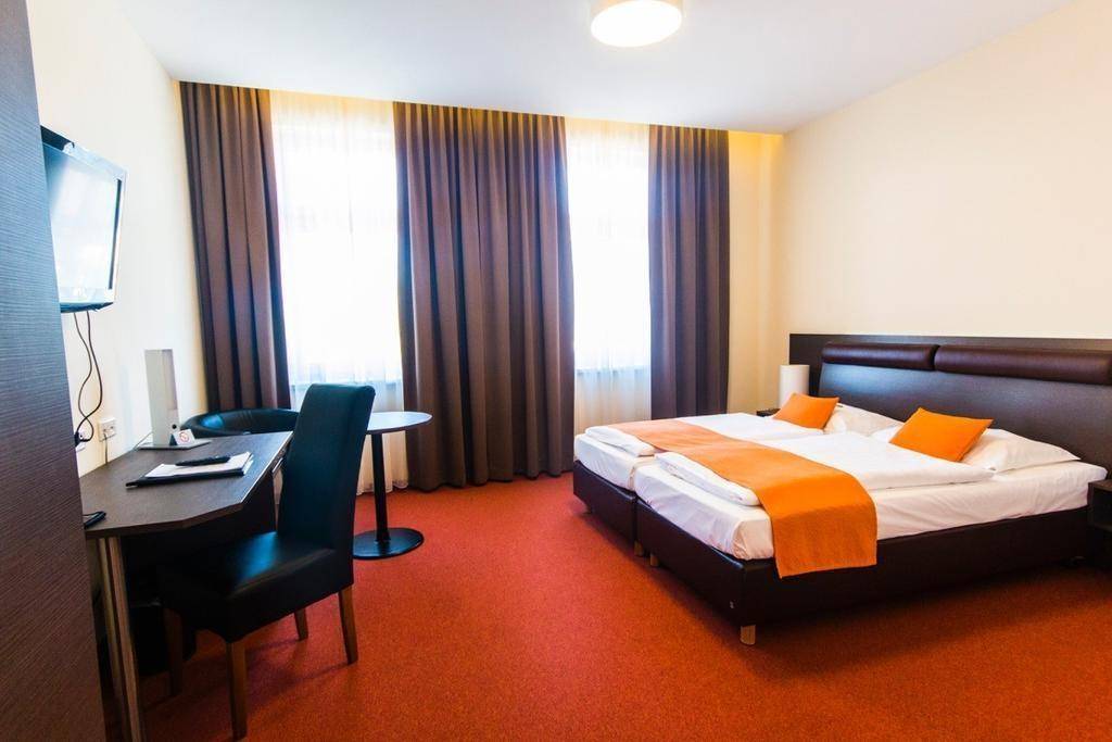 Helles Schlafzimmer mit zwei Einzelbetten, Schreibtisch und orangefarbenen Akzenten.