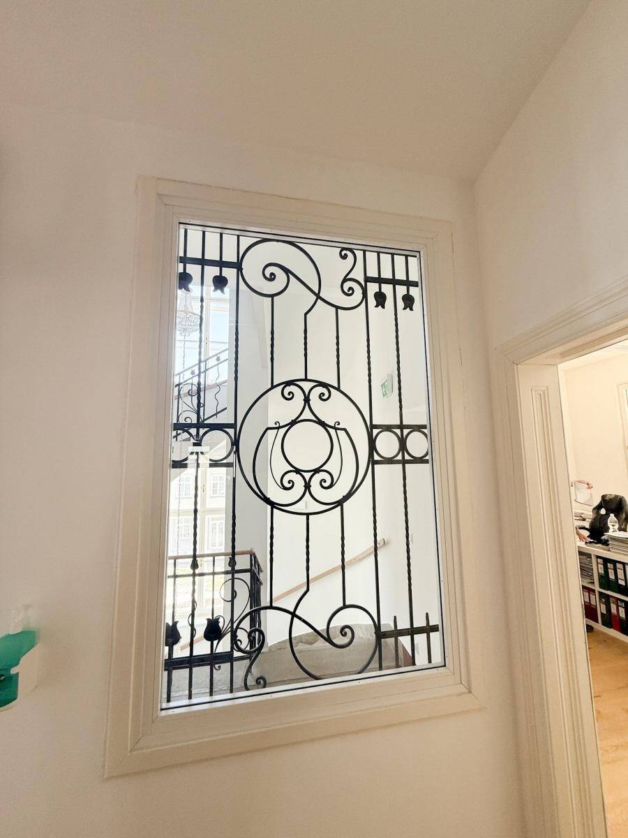 Detailansicht eines dekorativen Fensters mit kunstvollem Schmiedeeisen im Treppenhaus.