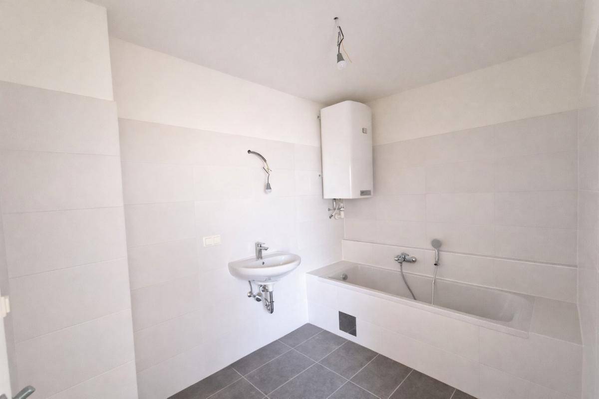 Modern gefliestes Badezimmer mit Badewanne, Waschbecken und Boiler, in neuwertigem Zustand.