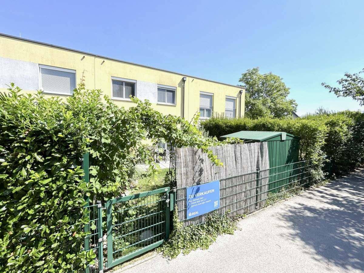Außenansicht des Hauses mit umzäuntem Gartenbereich und grüner Hecke.