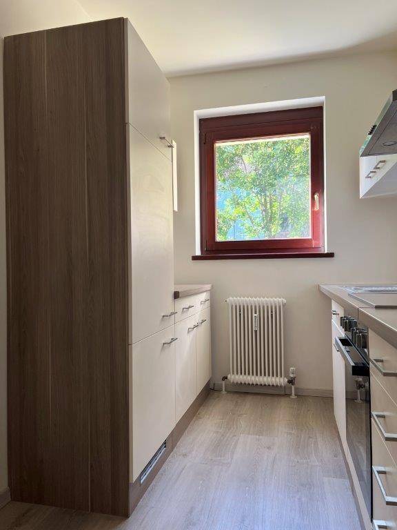 Helle Küche mit modernen Holz- und Weißfronten, ausgestattet mit einem Fenster und Heizkörper.