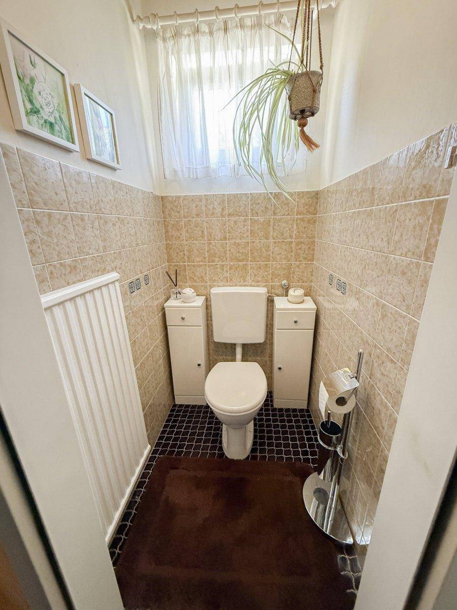Kleines Gäste-WC mit beigen Fliesen, Fenster und einfacher Ausstattung.