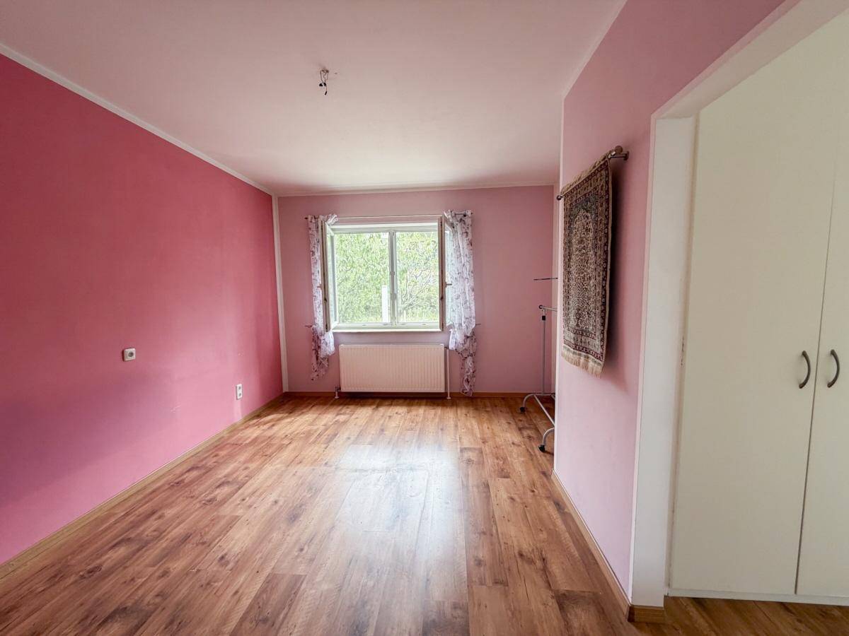 Schlafzimmer mit rosa Wänden, Laminatboden und großem Fenster mit Blick ins Grüne.