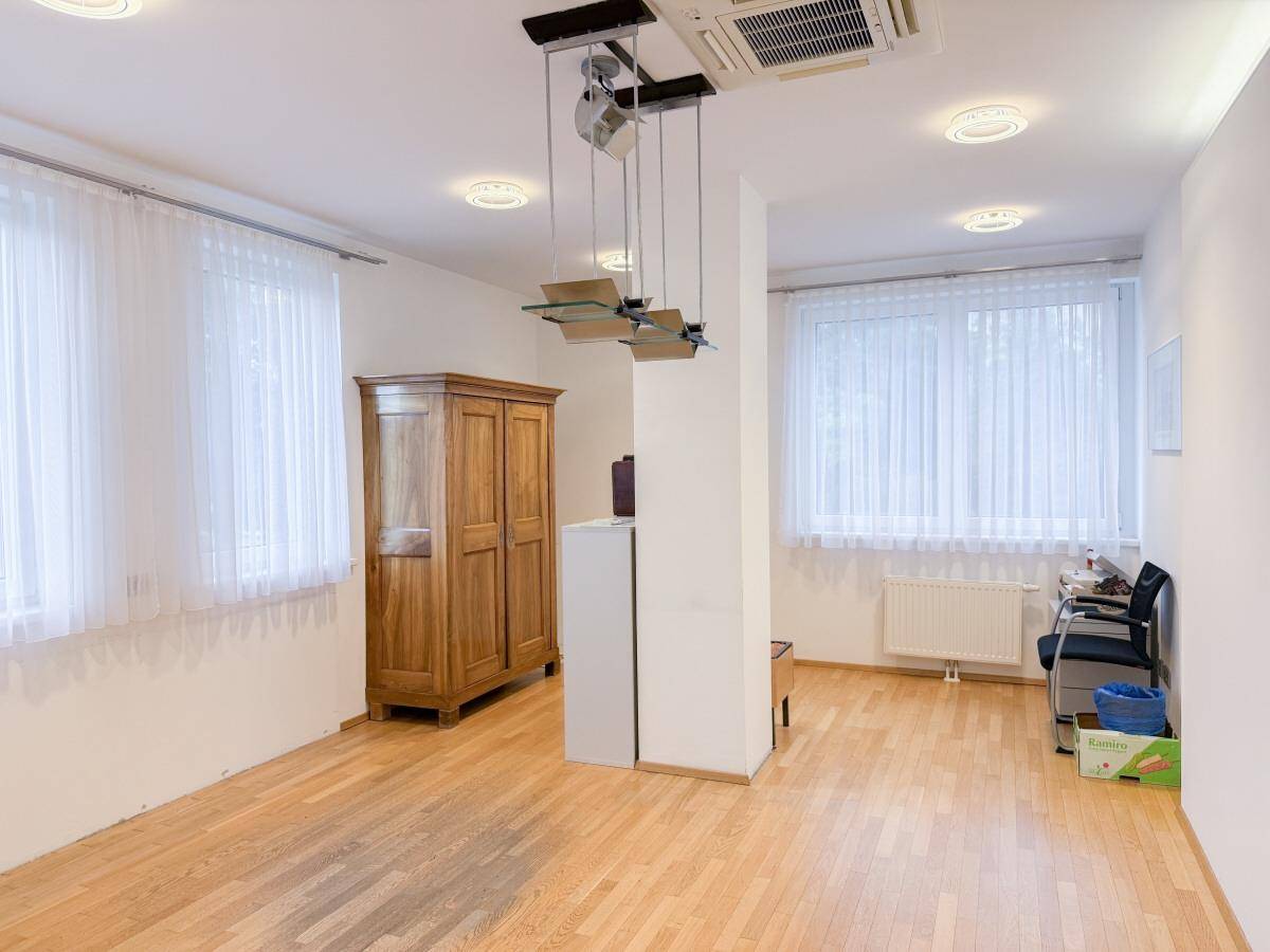 Geräumiger Büroraum mit Holzboden, zwei großen Fenstern und einem Holzschrank.