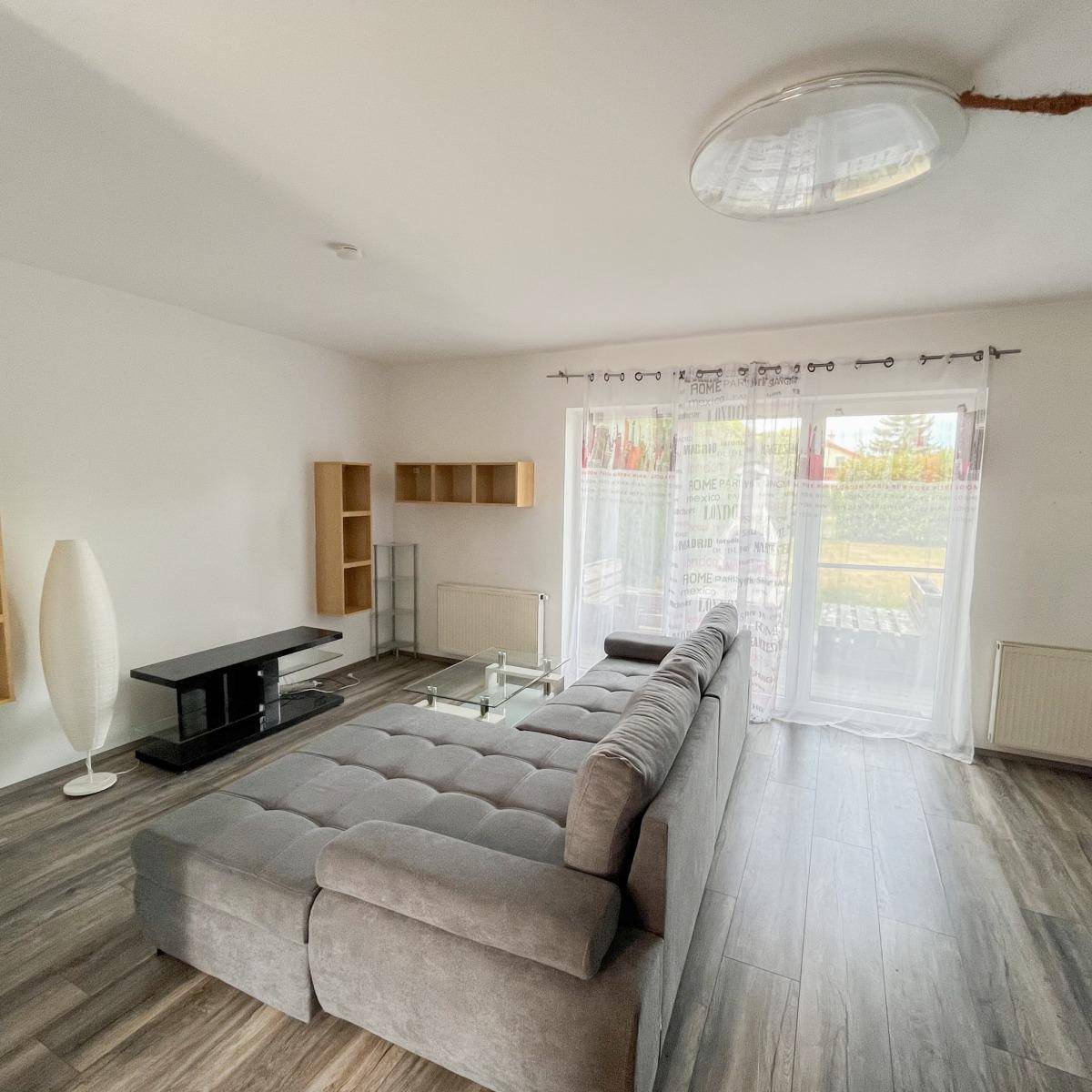 Helles Wohnzimmer mit großem Sofa, Laminatboden und Zugang zu einem Außenbereich.