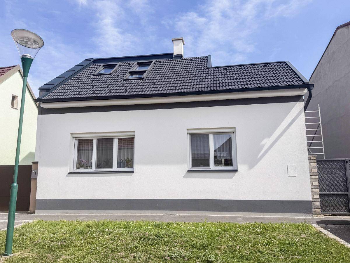 Vorderansicht eines modernen Einfamilienhauses mit weißer Fassade, dunklem Ziegeldach und Rasenfläche.