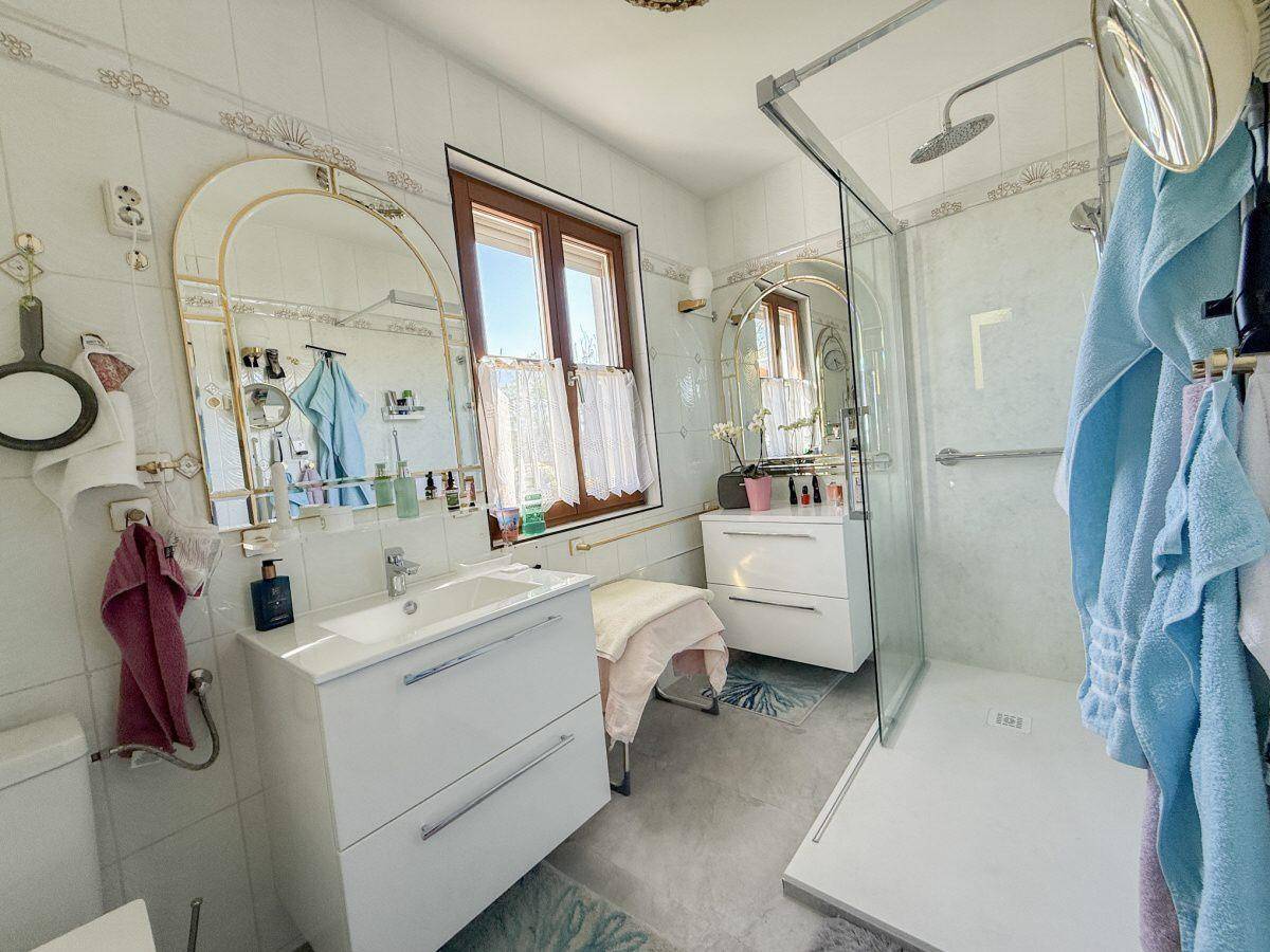 Helles Badezimmer mit moderner begehbarer Dusche, Einzelwaschbecken und einem Fenster.