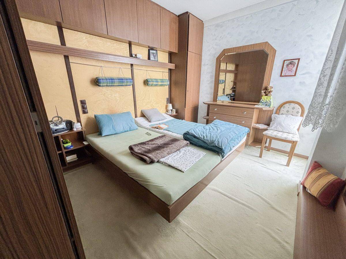 Schlafzimmer mit zwei Einzelbetten, Einbauschränken und einem Schminktisch mit Spiegel.
