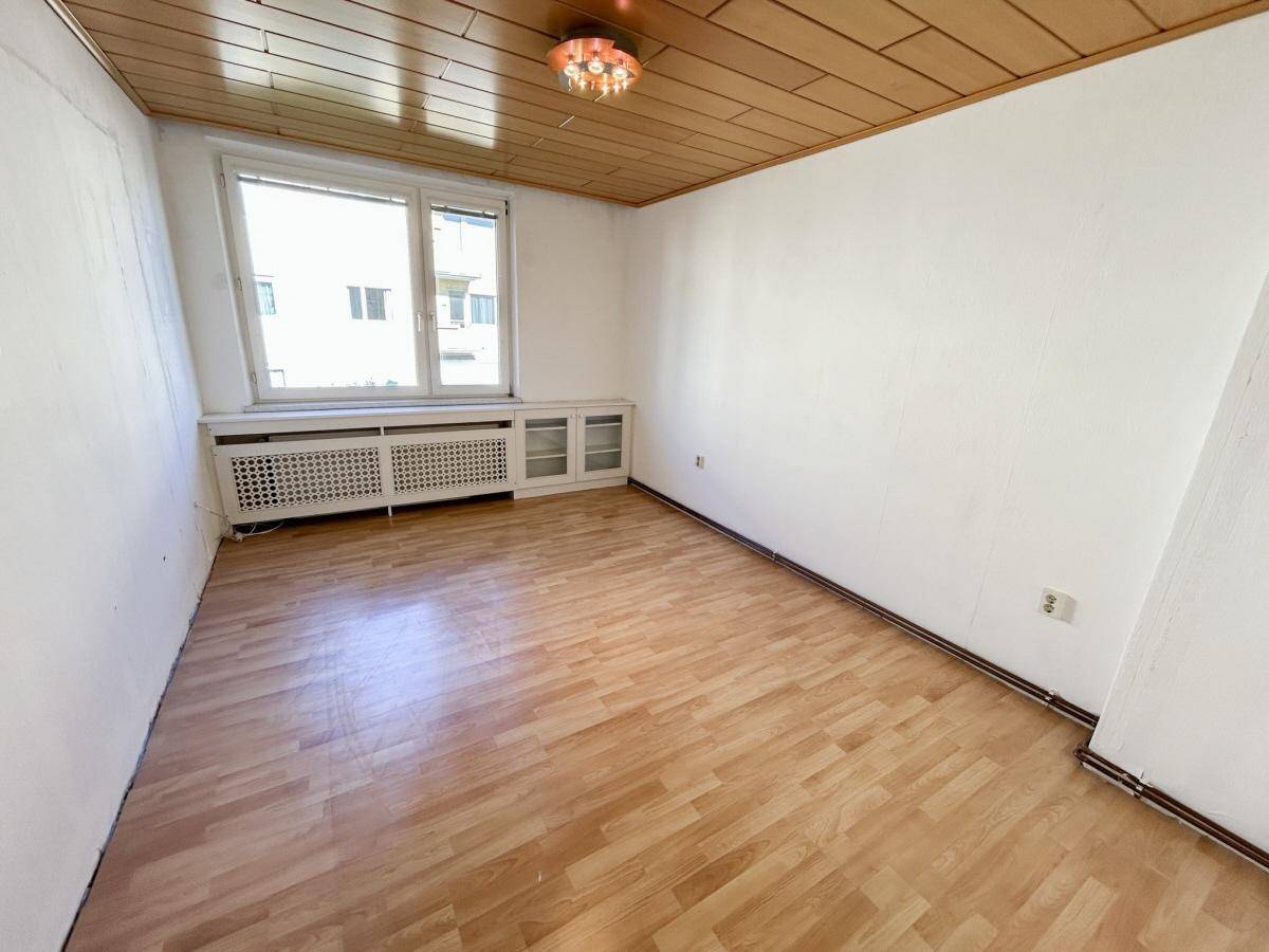 Helles Zimmer mit Laminatboden, Holzdecke und großem Fenster, das viel Tageslicht hereinlässt.