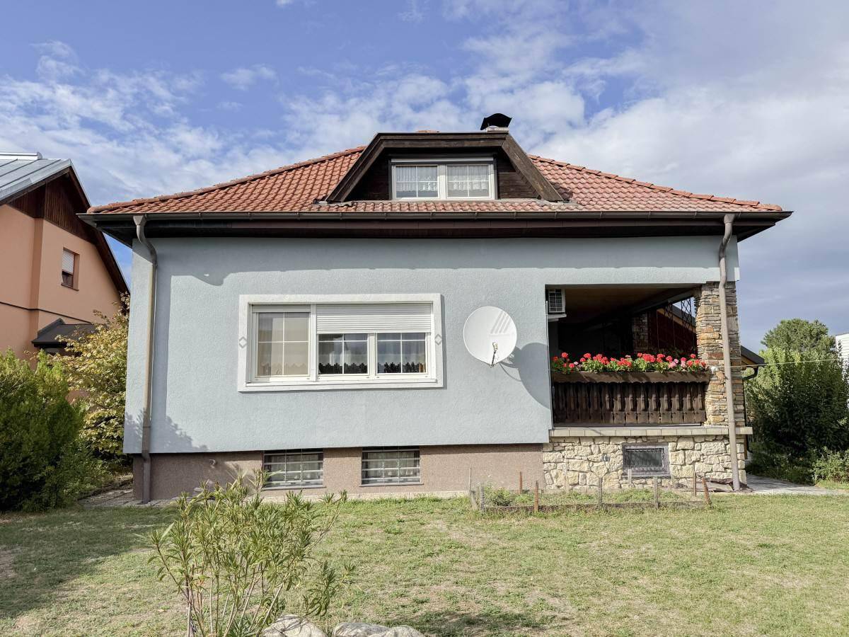 Rückansicht des Hauses mit überdachtem Balkon, Satellitenschüssel und einem gepflegten Gartenbereich.