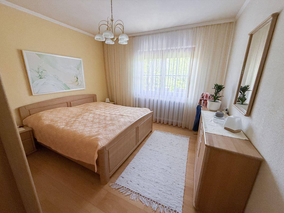 Gemütliches Schlafzimmer mit Holzbett, Parkettboden und großem Fenster.