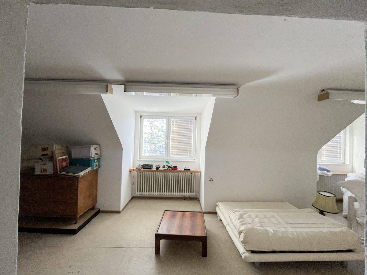 Heller Dachbodenraum mit schrägen Wänden, Fenster und einfacher Einrichtung.