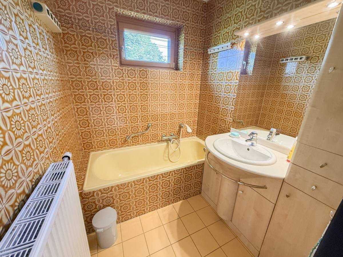 Badezimmer im 80er-Jahre-Stil mit gemusterten Fliesen, Badewanne und Fenster, charmant und funktional.