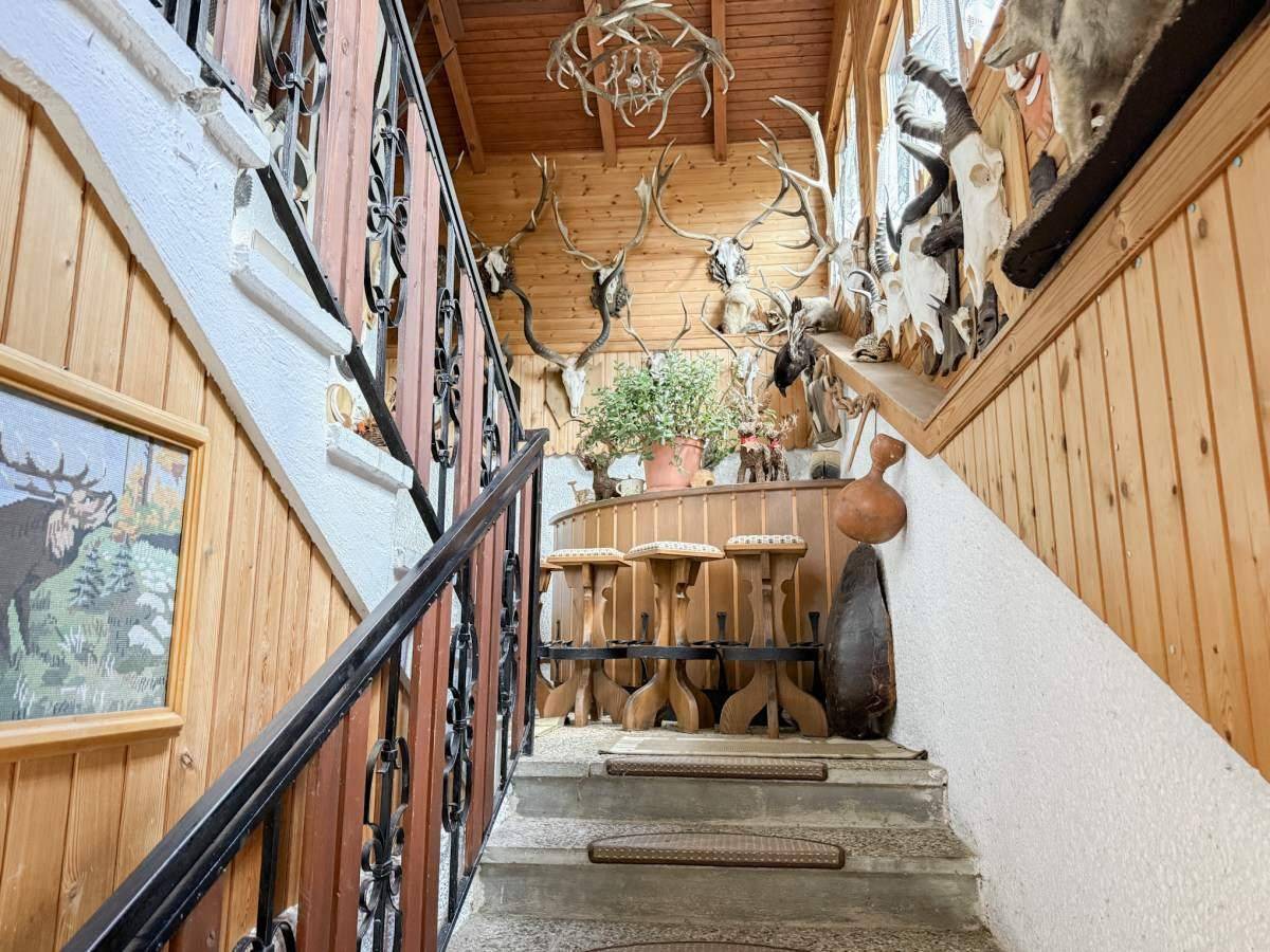Treppenaufgang mit Holzvertäfelung, schmiedeeisernem Geländer und Jagdtrophäen.