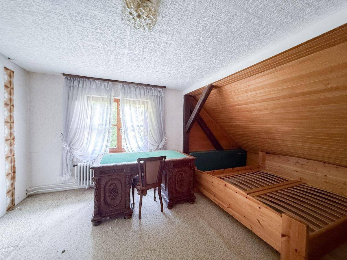 Schlafzimmer mit Holzbettrahmen, antikem Schreibtisch und schräger Holzverkleidung an der Wand.
