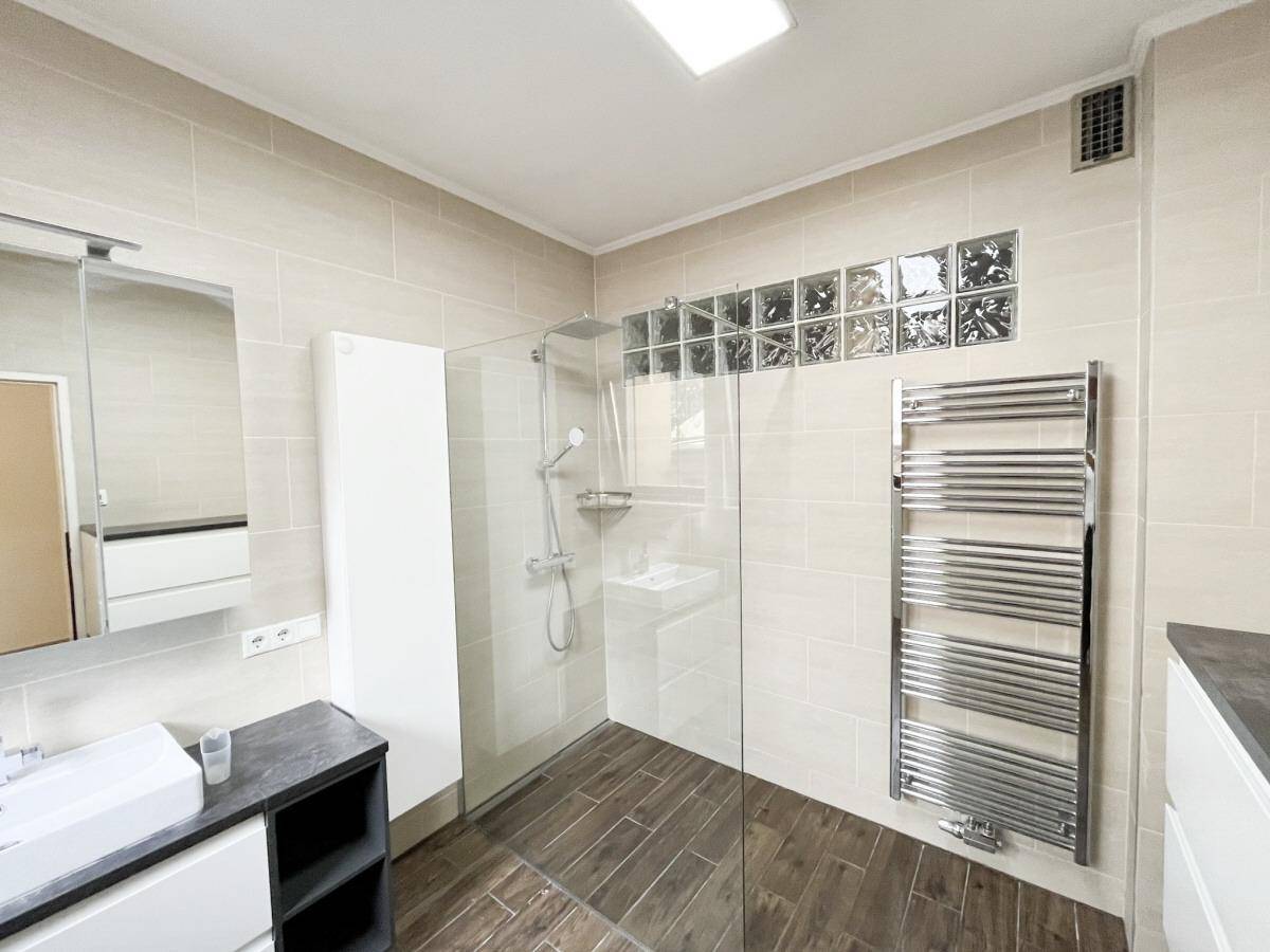 Helles Badezimmer mit begehbarer Dusche, Handtuchheizkörper und modernen Armaturen.