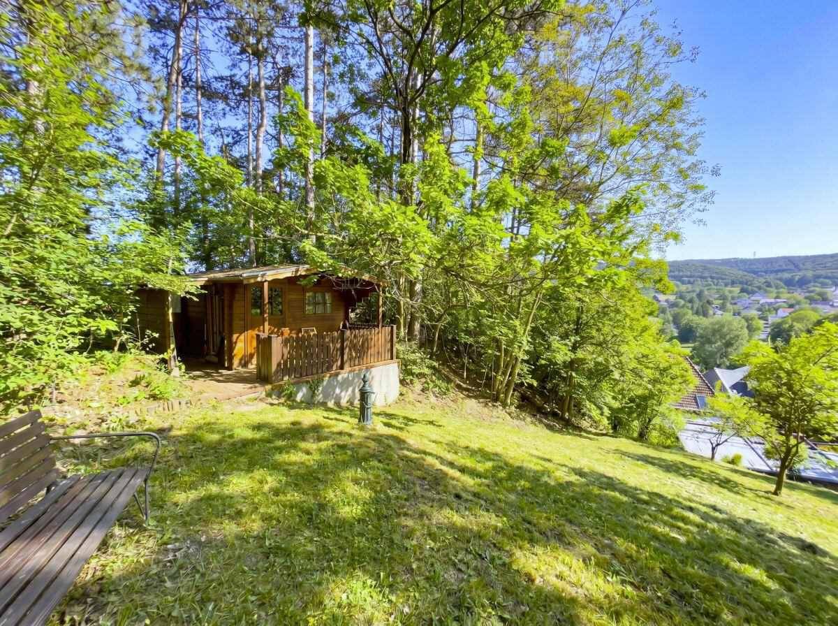 Naturbelassener Gartenbereich mit Holzhütte und Sitzbank, umgeben von Bäumen und Blick ins Tal.