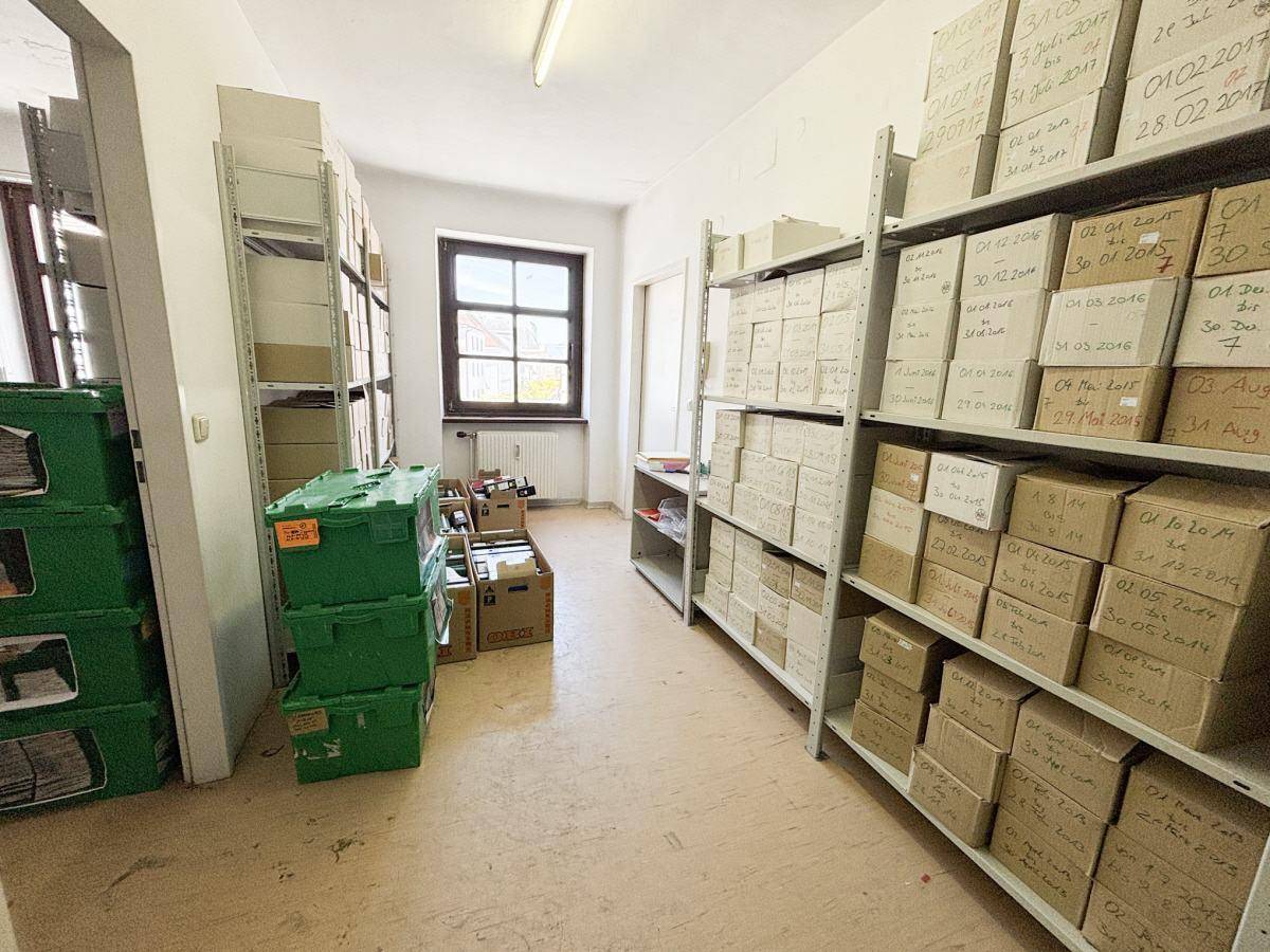 Archivraum mit hohen Regalen voller Kartons und Akten, beleuchtet durch ein Fenster.