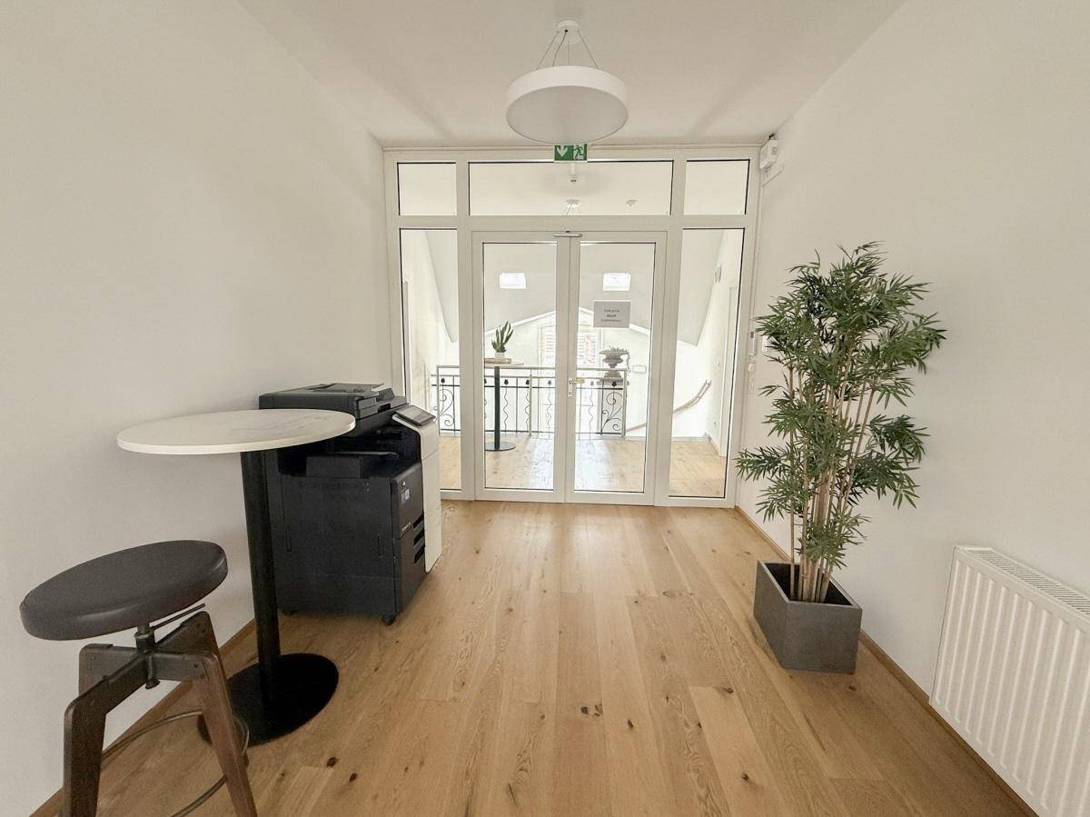 Heller Bürobereich mit Holzfußboden und großen Glastüren, die zu einem Balkon führen.