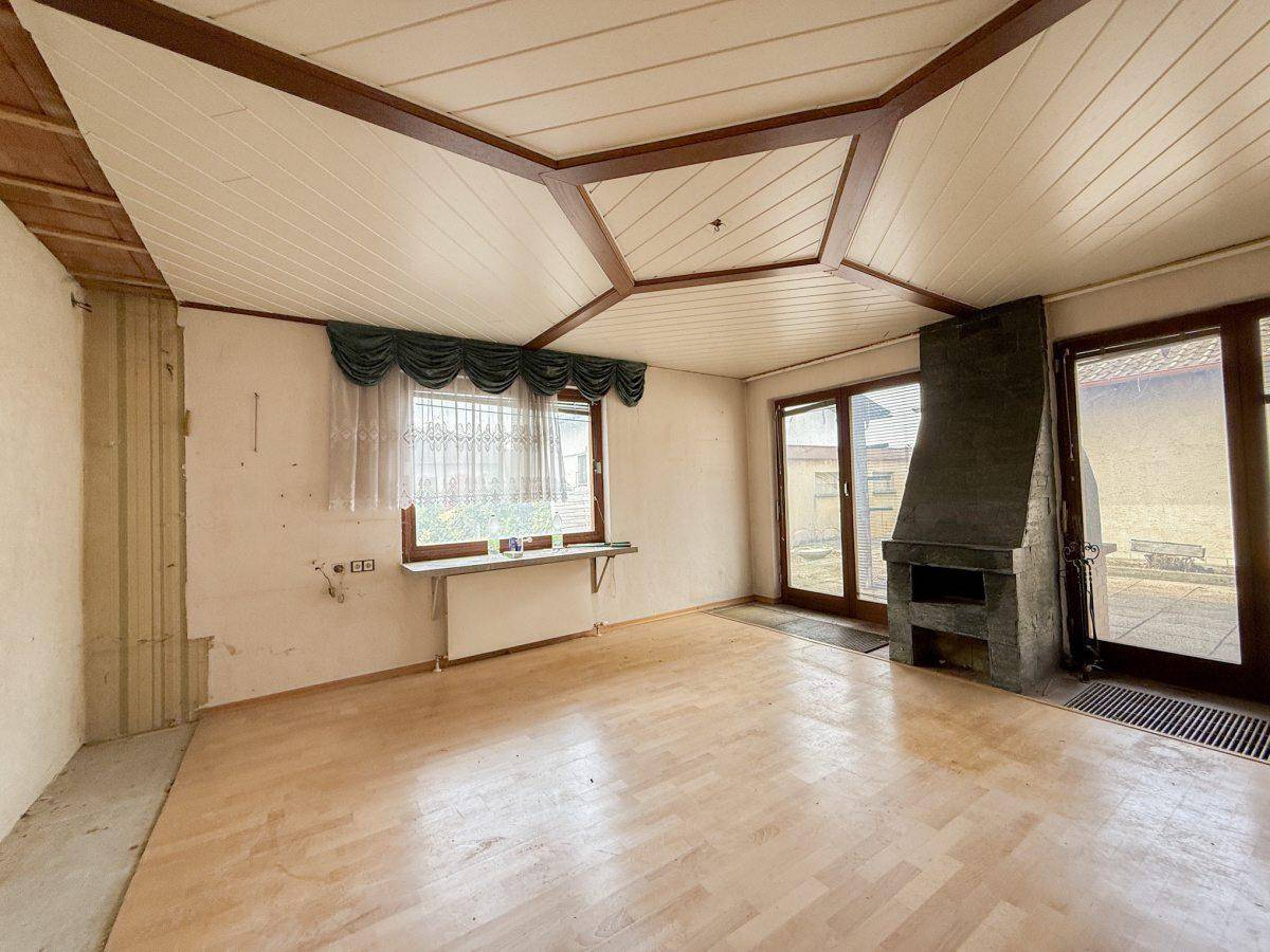 Wohnzimmer mit Holzboden, Kamin und Zugang zur Terrasse, unter einer Holzdecke.