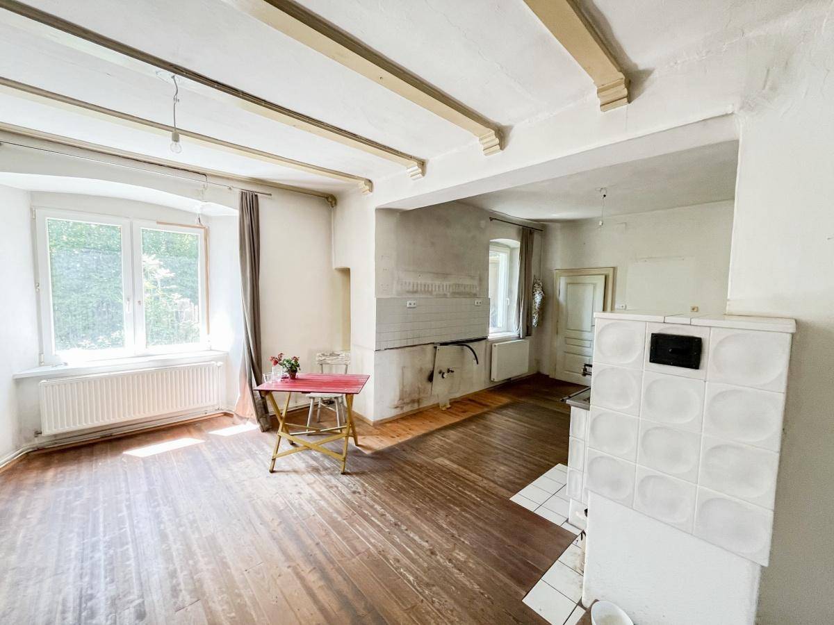Heller Wohnbereich mit Holzboden, großem Fenster und traditionellem Kachelofen.