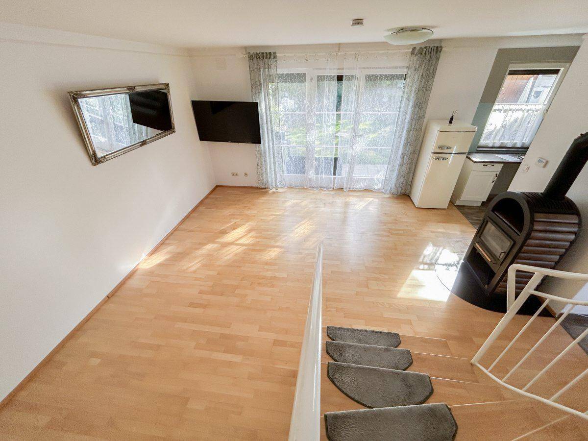 Helles Wohnzimmer mit Holzboden, Kaminofen und Zugang zum Gartenbereich.