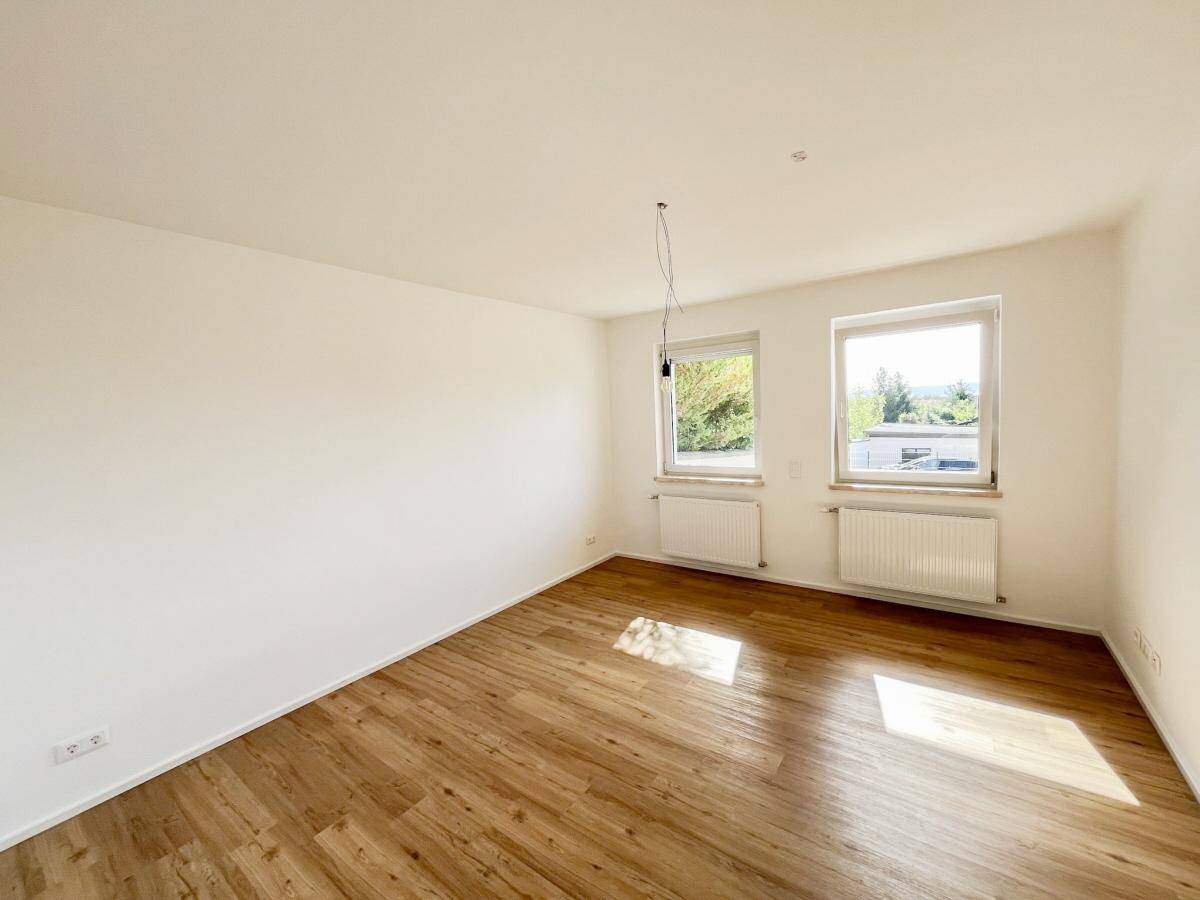 Helles Zimmer mit Holzfußboden und zwei Fenstern, bereit zur individuellen Gestaltung.