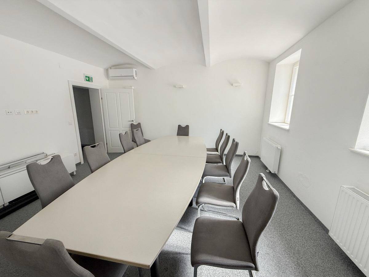 Geräumiger Konferenzraum mit Teppichboden, langer Tafel, Klimaanlage und hohen Decken.