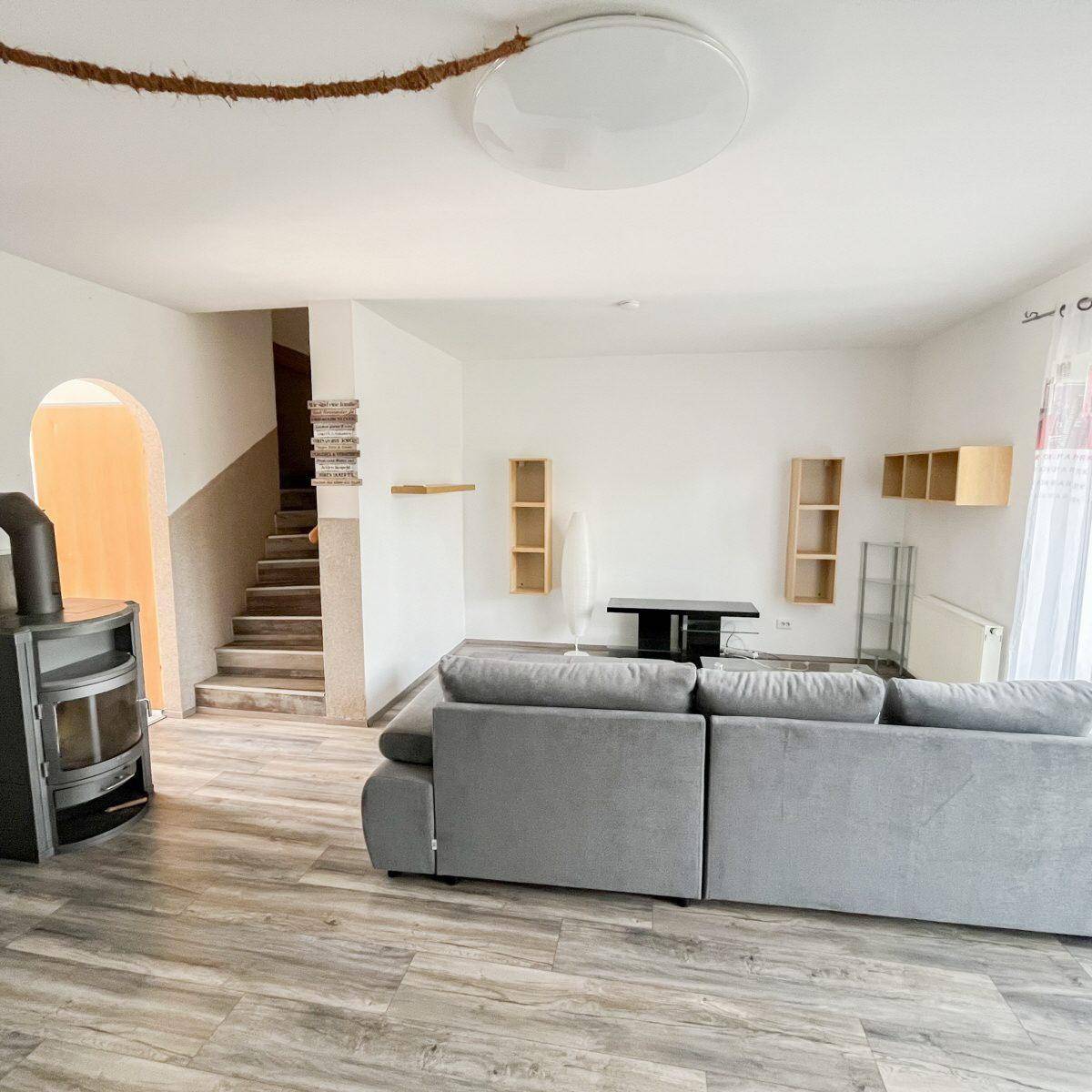 Gemütliches Wohnzimmer mit Holzofen, großem Sofa und Laminatboden, führt zur Treppe.