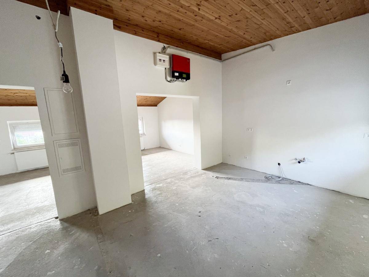Rohbau-Raum mit Holzbalkendecke und Betonboden, offen zu angrenzenden Bereichen.