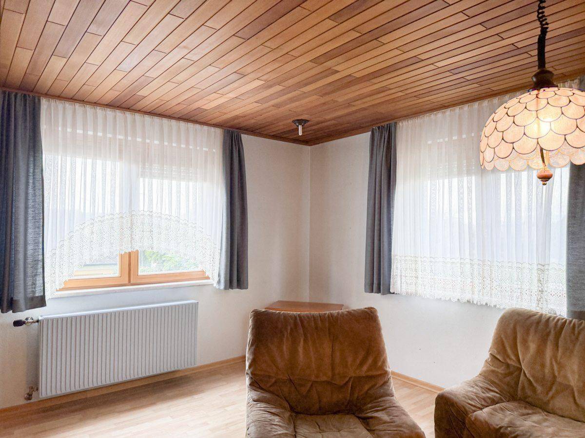 Gemütlicher Wohnraum mit zwei Sesseln, Holzdecke, Holzfußboden und großen Fenstern.